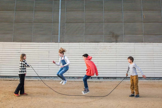 Niños participando en juegos callejeros tradicionales con cuerda para saltar en un patio al aire libre