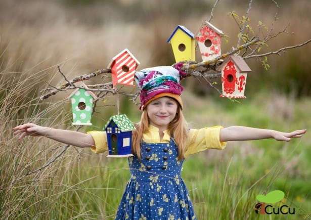 Niña sonriente con ramas y casas de pájaros de colores mostrando como hacer una casa para pájaros