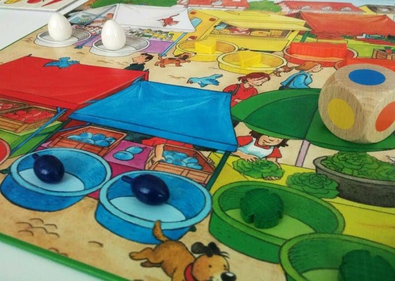 Tablero de juego colorido con piezas y dado de madera mostrando cómo jugar a Mi Primer Tesoro de Juegos