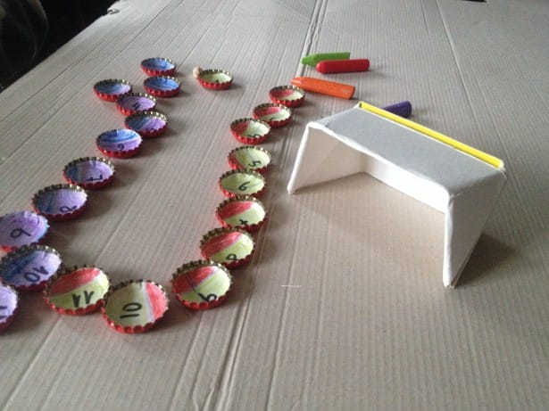 Material y setup casero para aprender como jugar a las chapas con niños usando chapas numeradas y un arco de papel