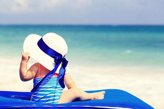 Bebé con sombrero blanco y vestido azul disfrutando la playa. Consejos para disfrutar la playa con bebés