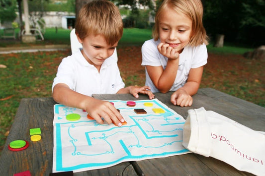 Niños aprendiendo cómo jugar El hilo de Ariadna paso a paso con tablero y fichas en mesa de madera