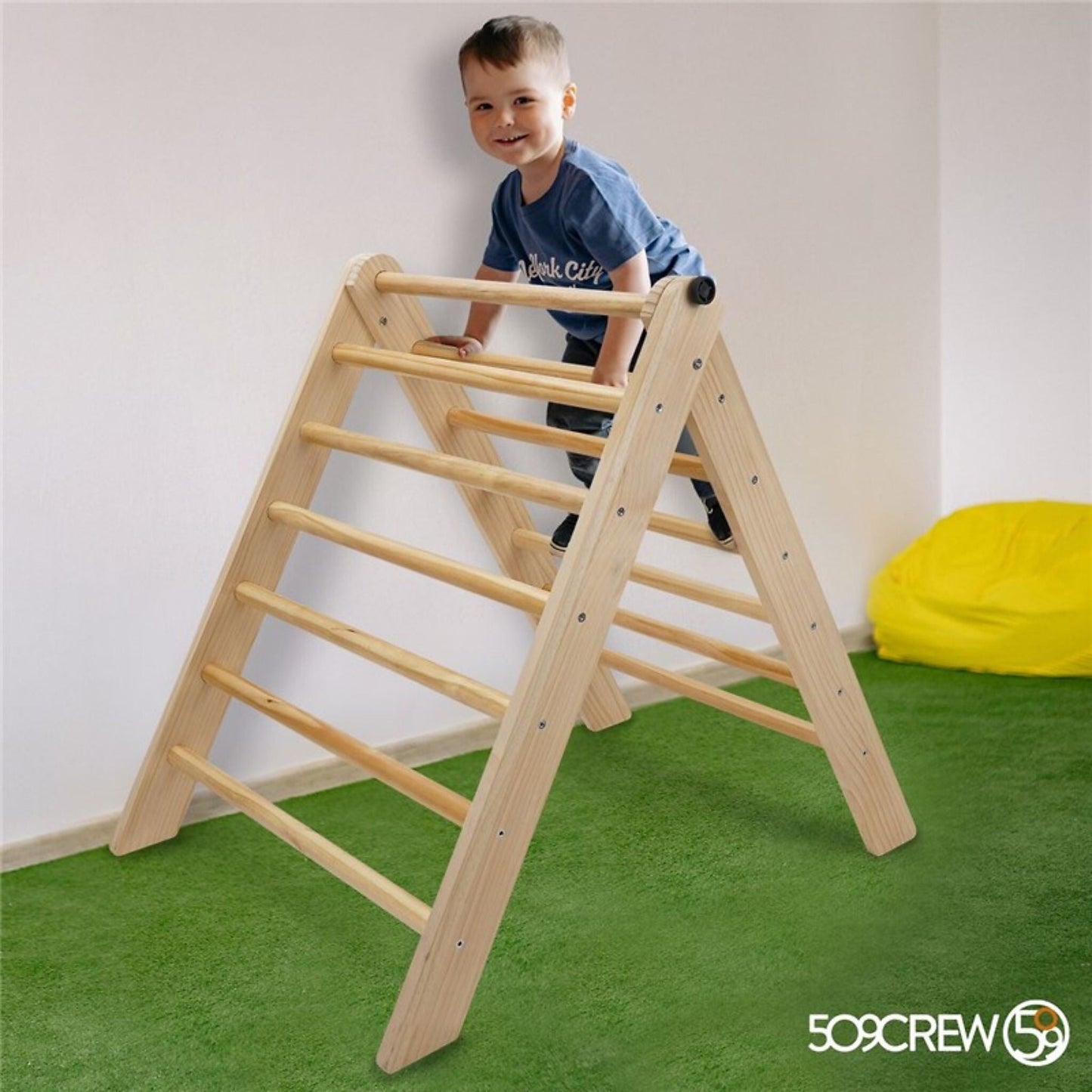 Niño jugando en triangulo de escalada Montessori de madera natural en habitación con suelo verde