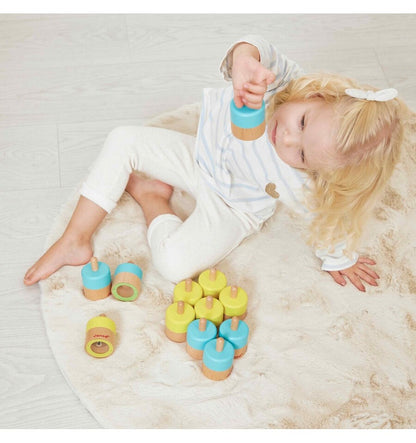Niña jugando con memo sonoro de madera Janod en colores azul y amarillo sobre alfombra clara